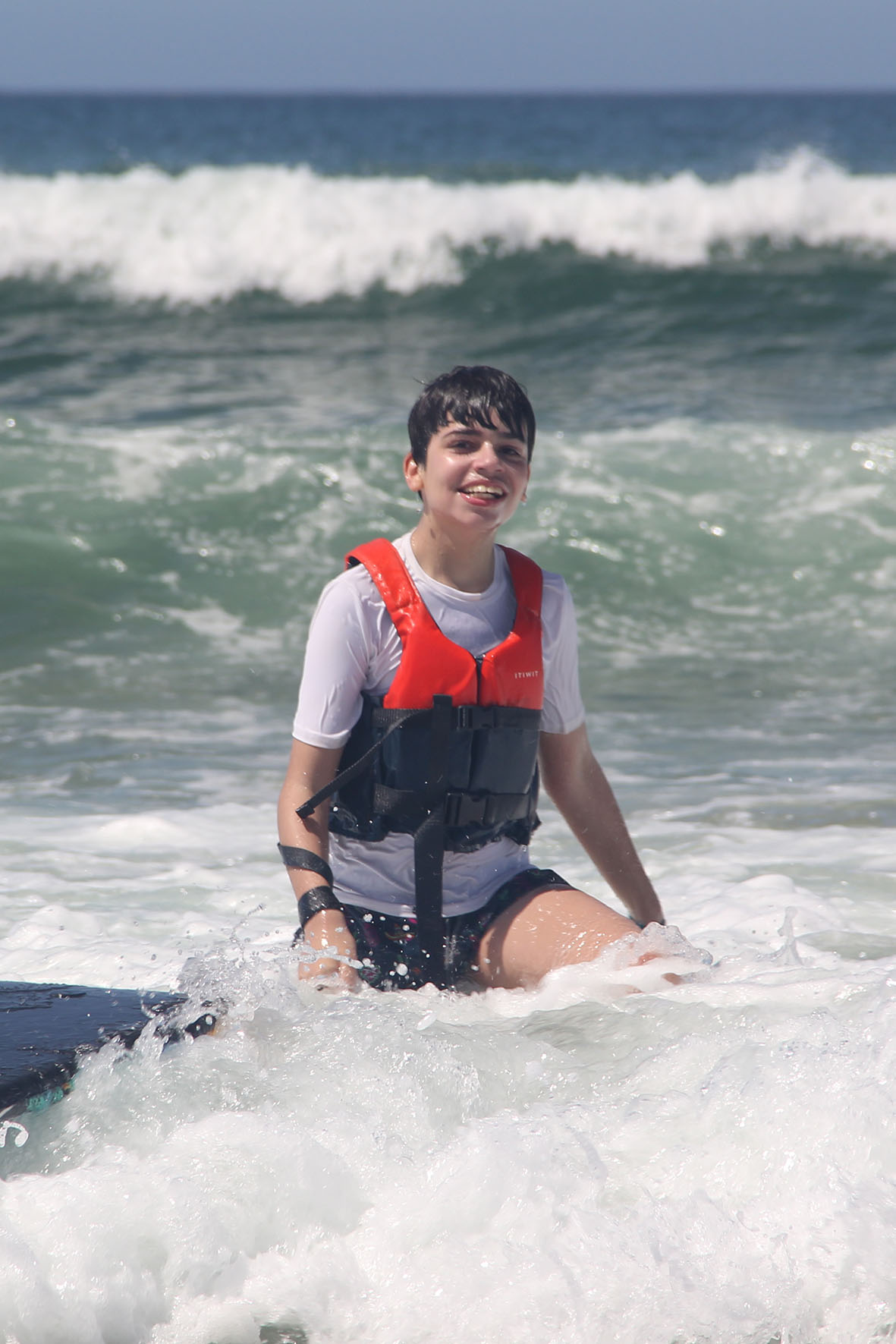 Alexandre, um rapaz de 14 anos, sentado na água do mar com um colete salva-vidas laranja