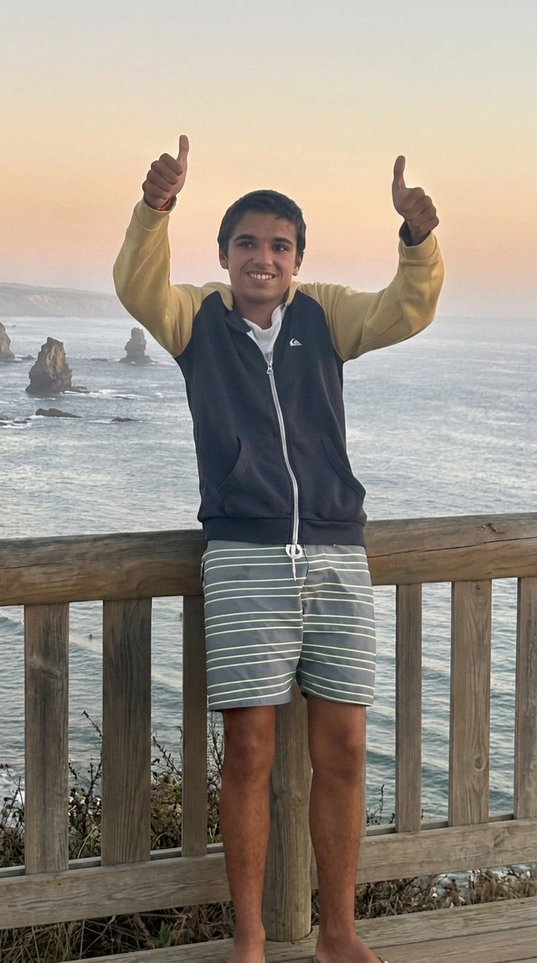 Henrique, o Kike, a fazer um gesto de positivo com o mar ao fundo